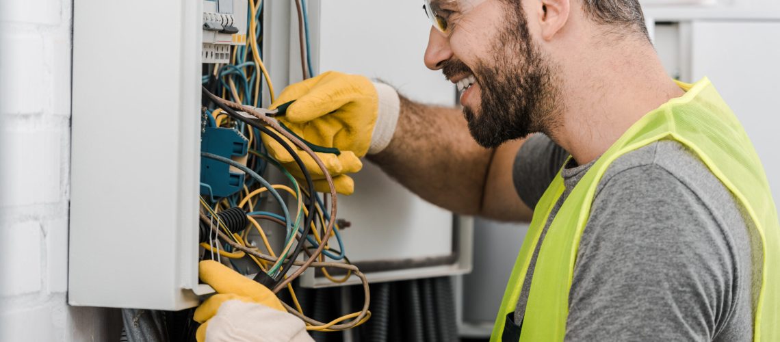 Side,View,Of,Smiling,Handsome,Electrician,Repairing,Electrical,Box,With